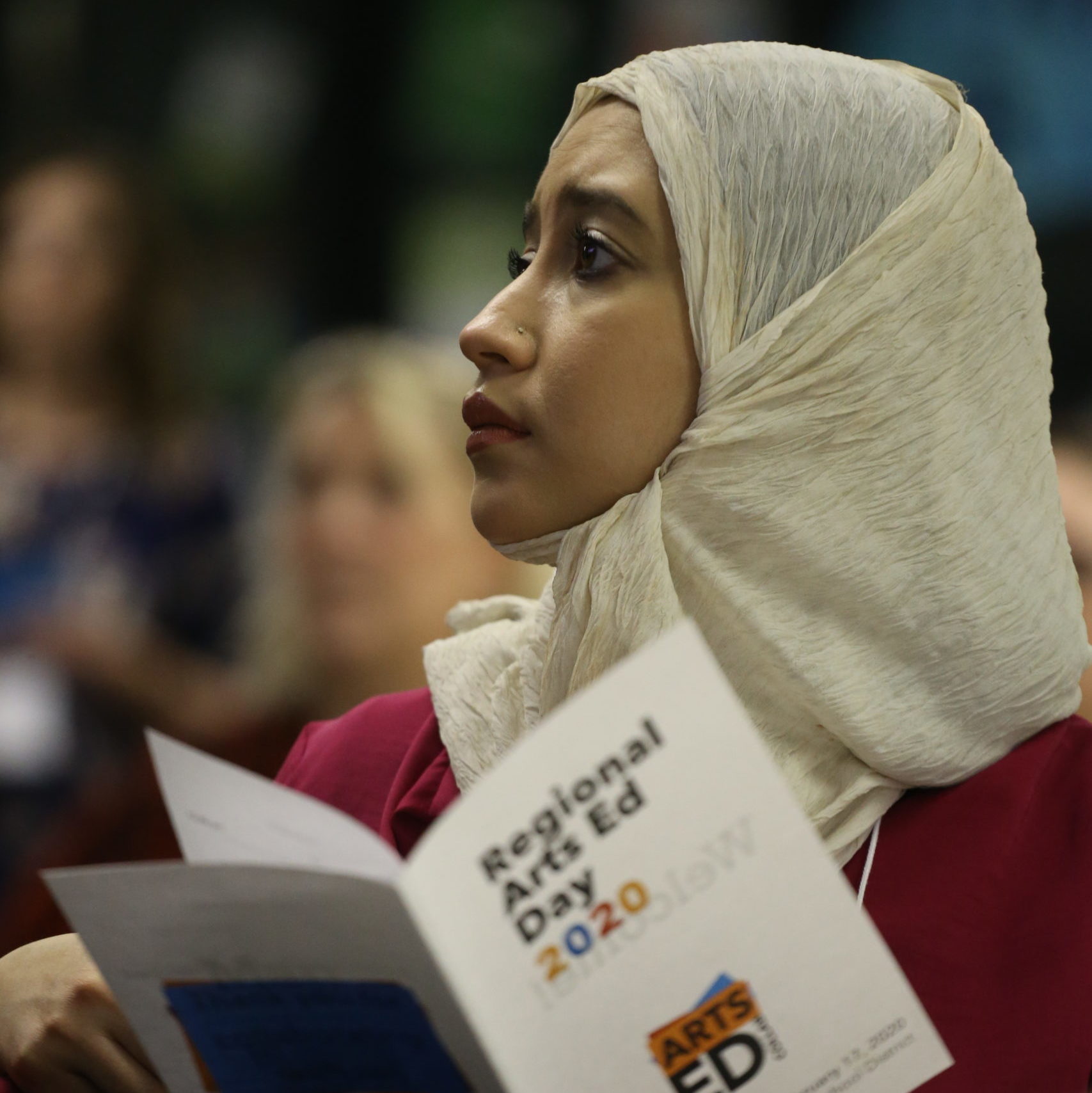 An educator wearing a hijab holds a Regional Arts Ed Day program.
