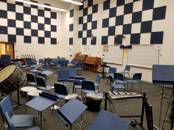 A large music room full of plastic chairs, percussion instruments, and classical guitars with acoustic padding high on the walls.
