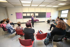 Author Sydelle Pearl discusses storytelling with arts educators seated in a circle in a large classroom with a blackboard on the wall.