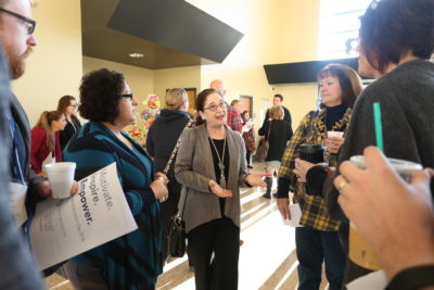 The image depicts a group of educators gathered around AEC Director Sarah Tambucci at RAED 2016