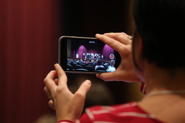 Closeup of someone's hands as they film a jazz ensemble on a smartphone.