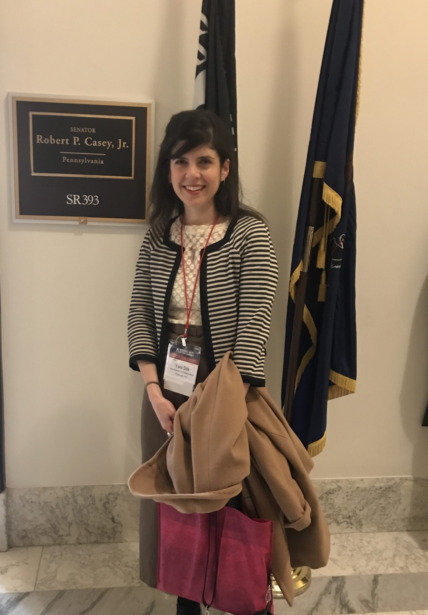 Yael stands in front of two flags next to Senator Casey's name plate outside his office in D.C.