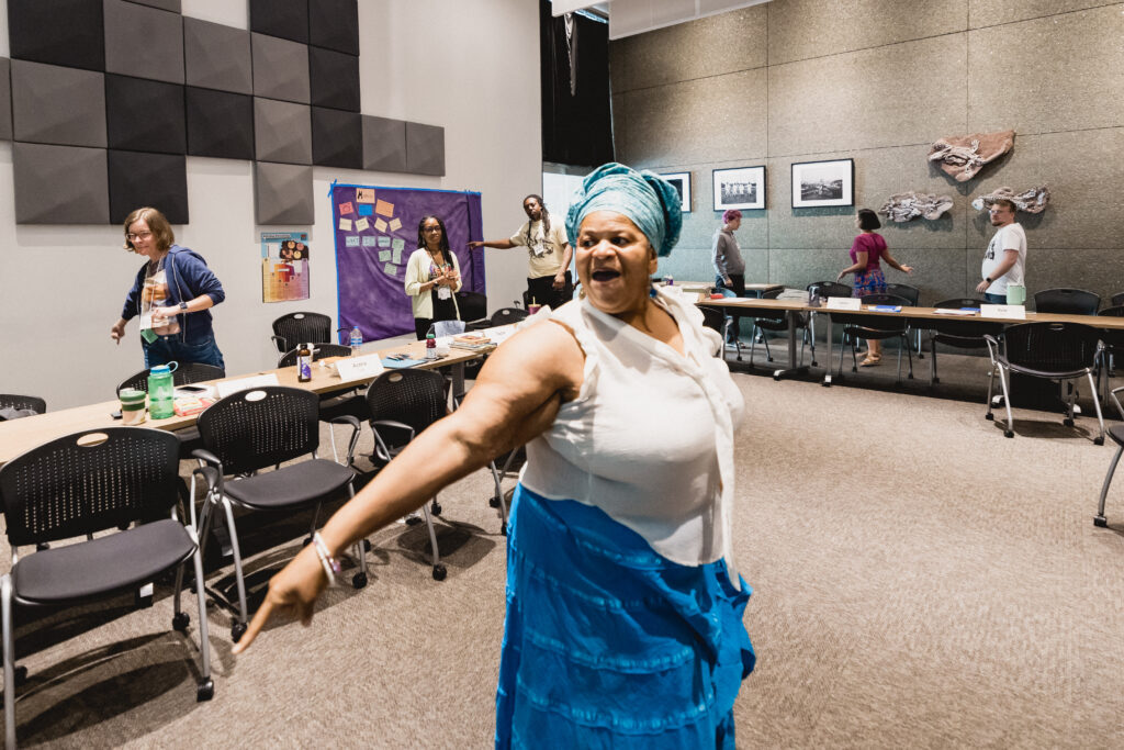 Woman stands in the forefront leading a group of people in a dance. 