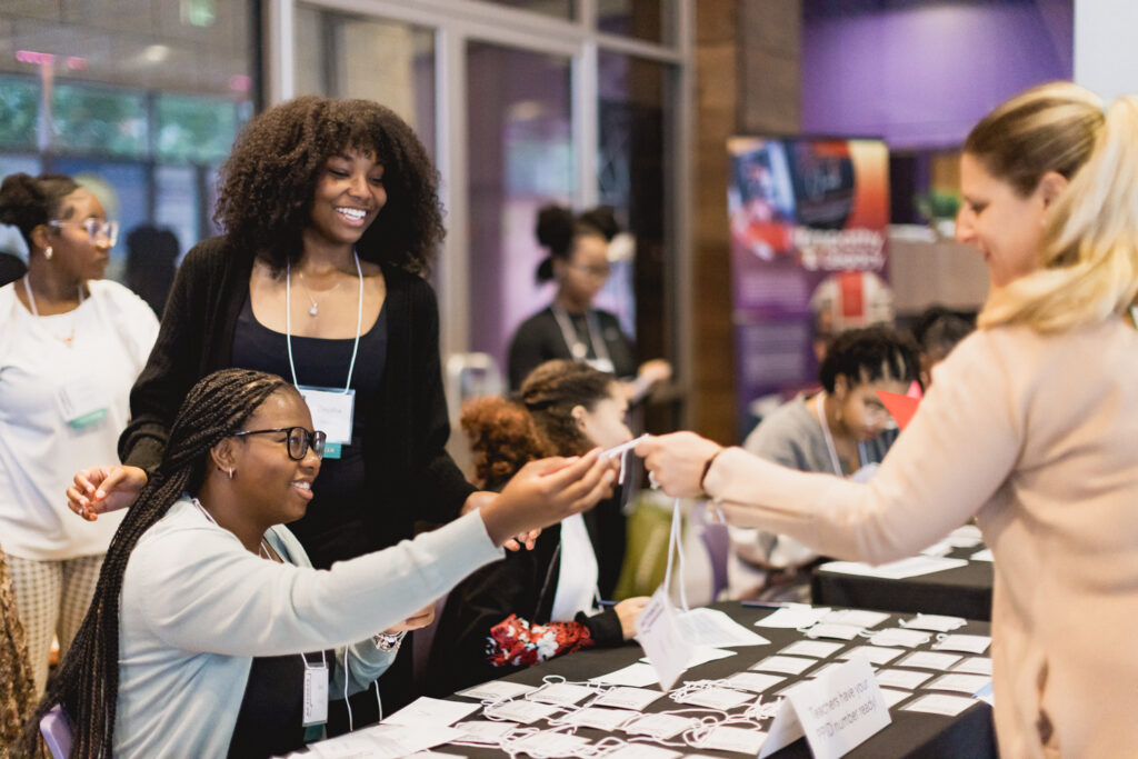 One person sits at a table with nametags, hands it to another person. 