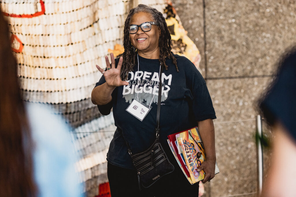 Woman stands in center of frame, waving.