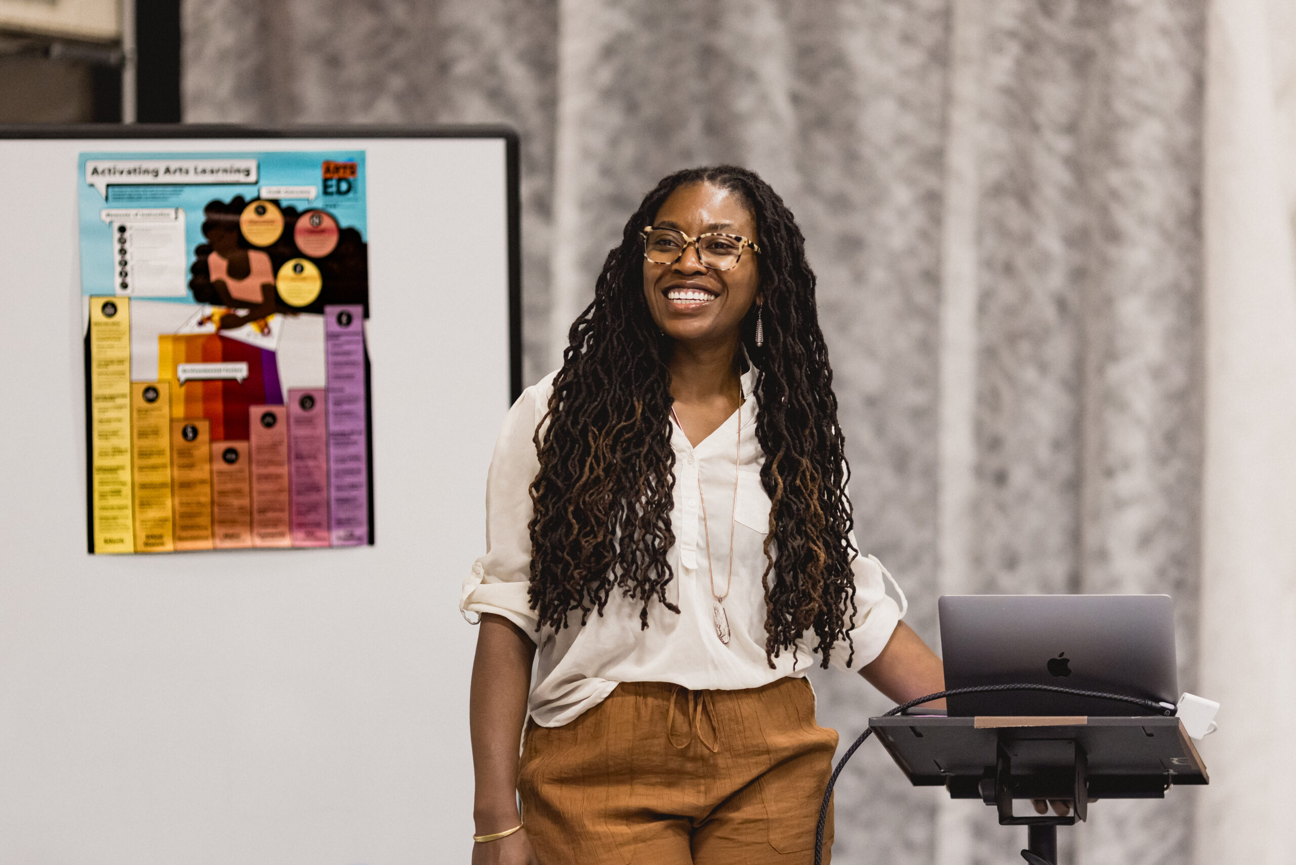 Person stands smiling in front of room by podium. 