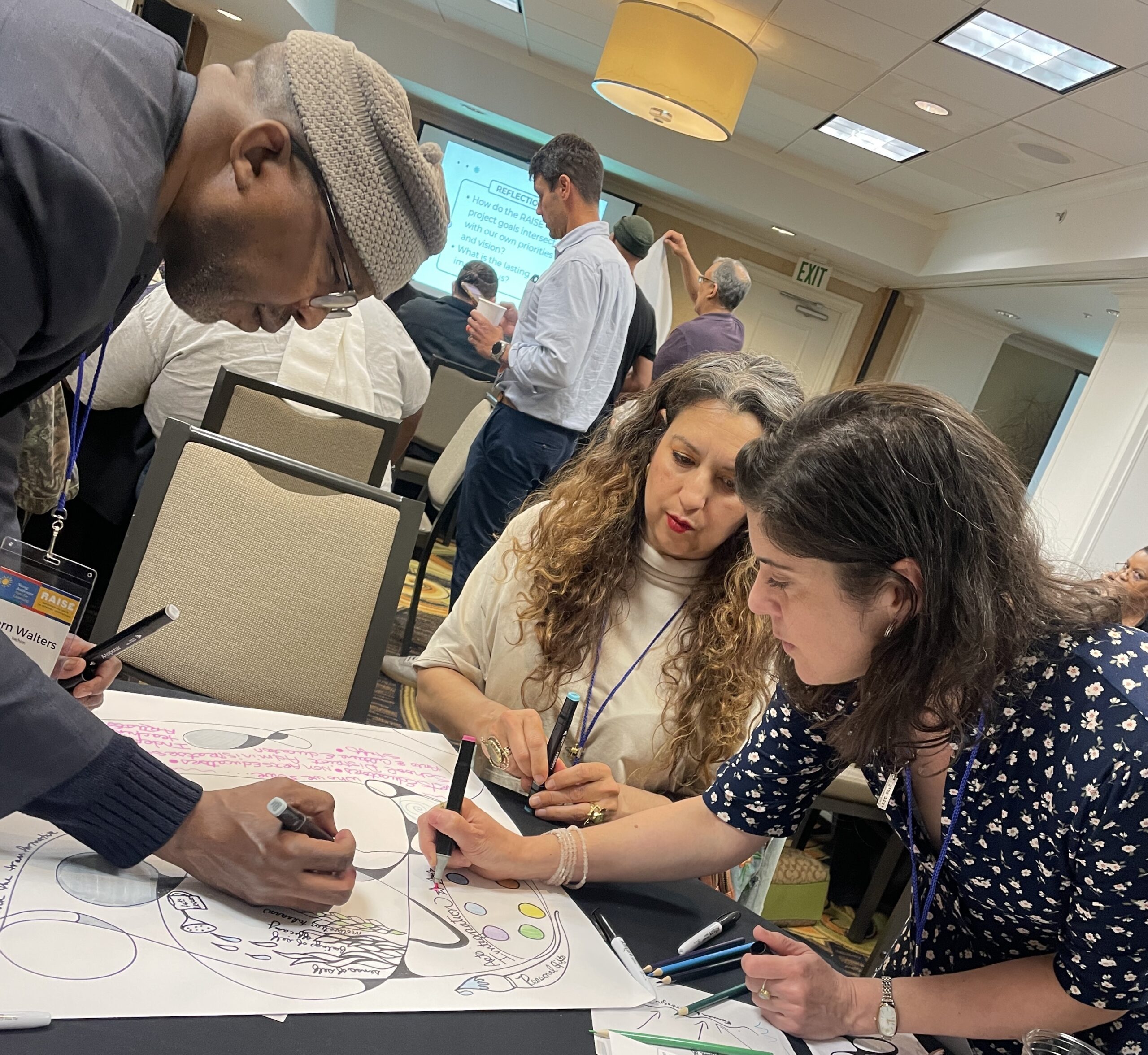 Three people stand around a table working on a poster together.