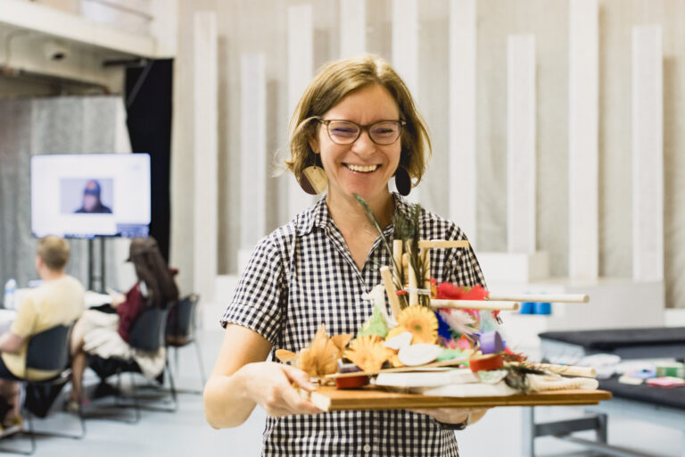 Smiling woman carries a tray of crafts.