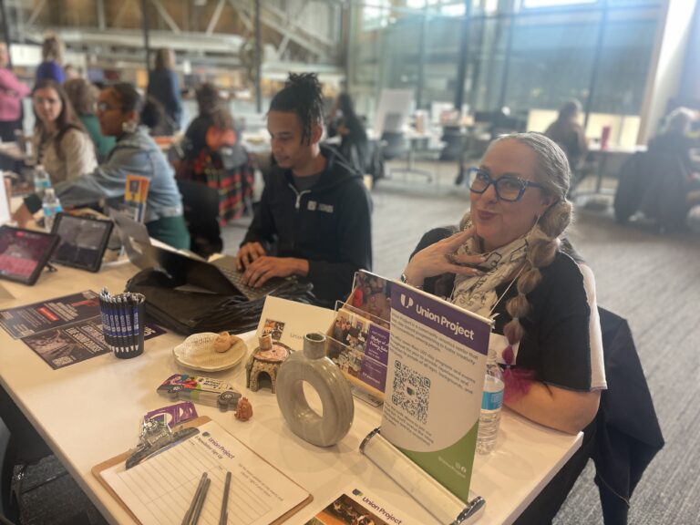 Group of people sit and smile at a table at the Arts Partner Fair.